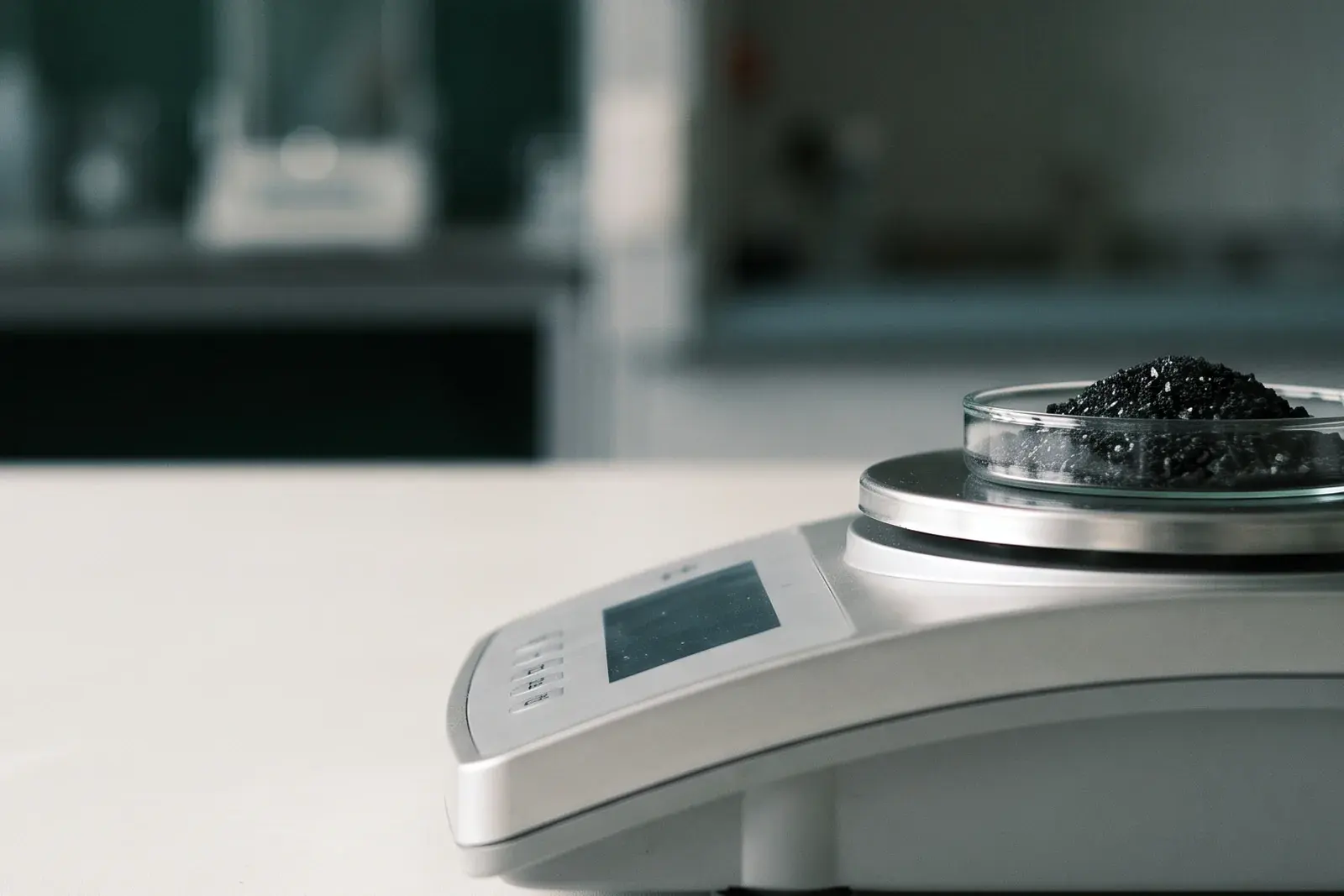 A heap of granular biochar on the pan of a precision analytical balance in a laboratory.
